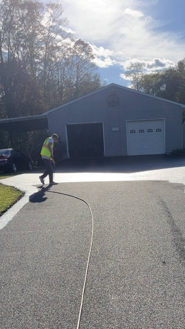 Crew member spraying sealcoat on a driveway